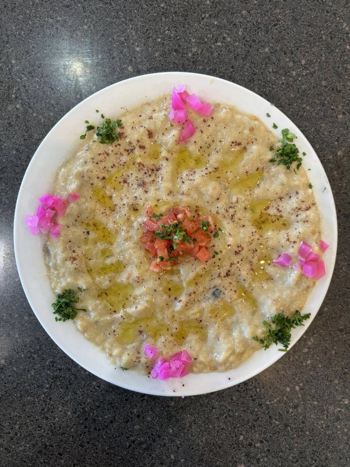 Baba ganoush Levantine cuisine appetizer of baked eggplant and sesame paste with herbs and olive oil on a concrete background