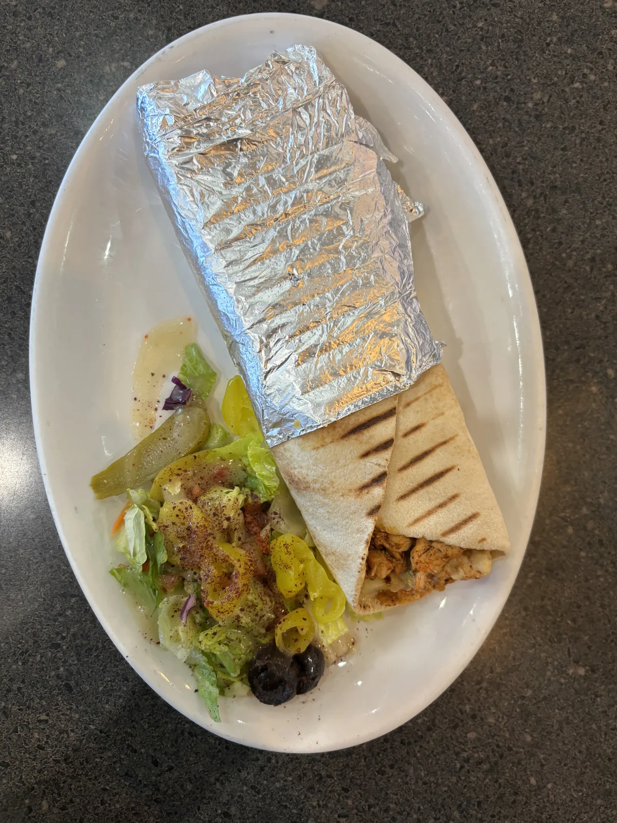 Close-up of a traditional Greek gyros wrap with grilled meat, fries, and vegetables in pita bread, resting on a rustic wooden table under warm natural light, evoking a cozy Mediterranean feel.